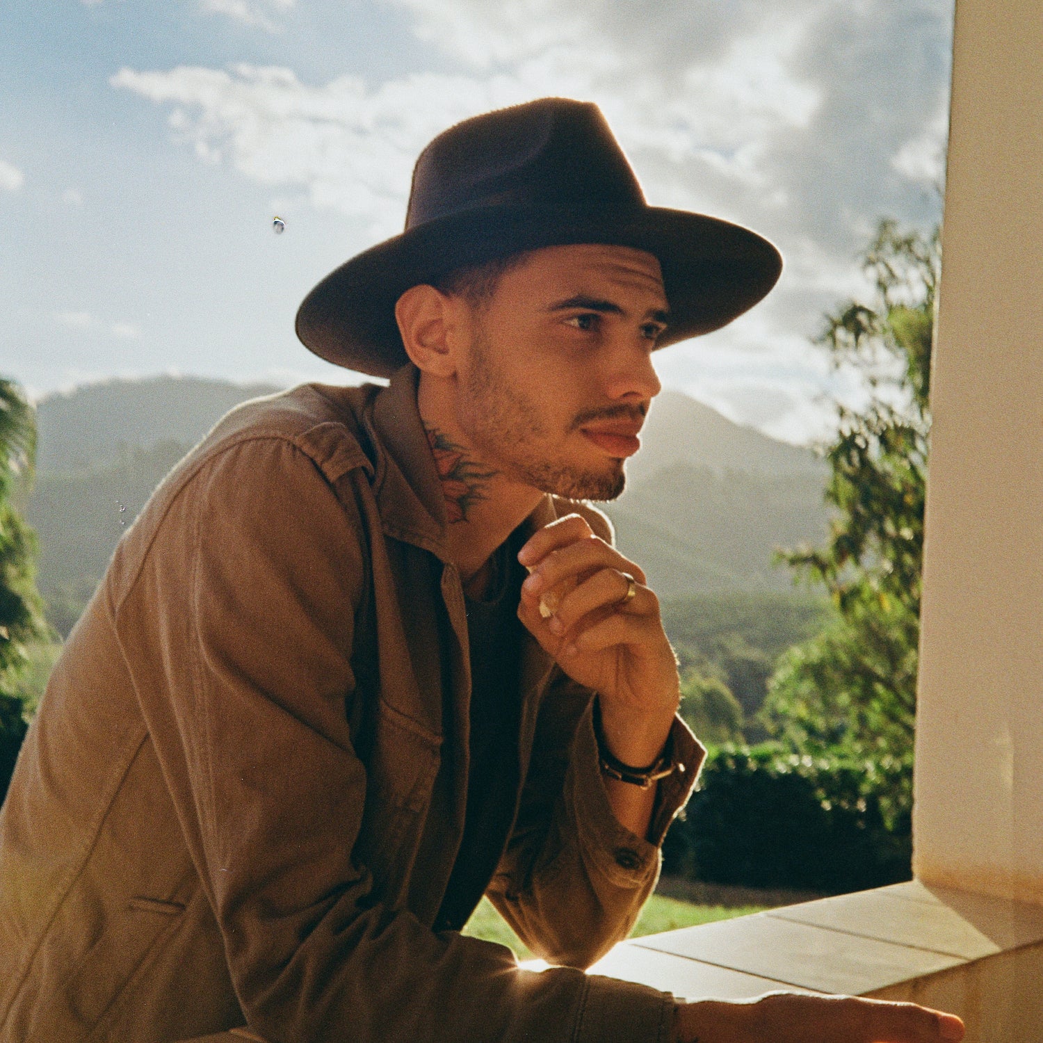 Douglas Condé - ogum cafe homem com chapeu preto com olhar pensativo com uma fazenda de cafe no fundo